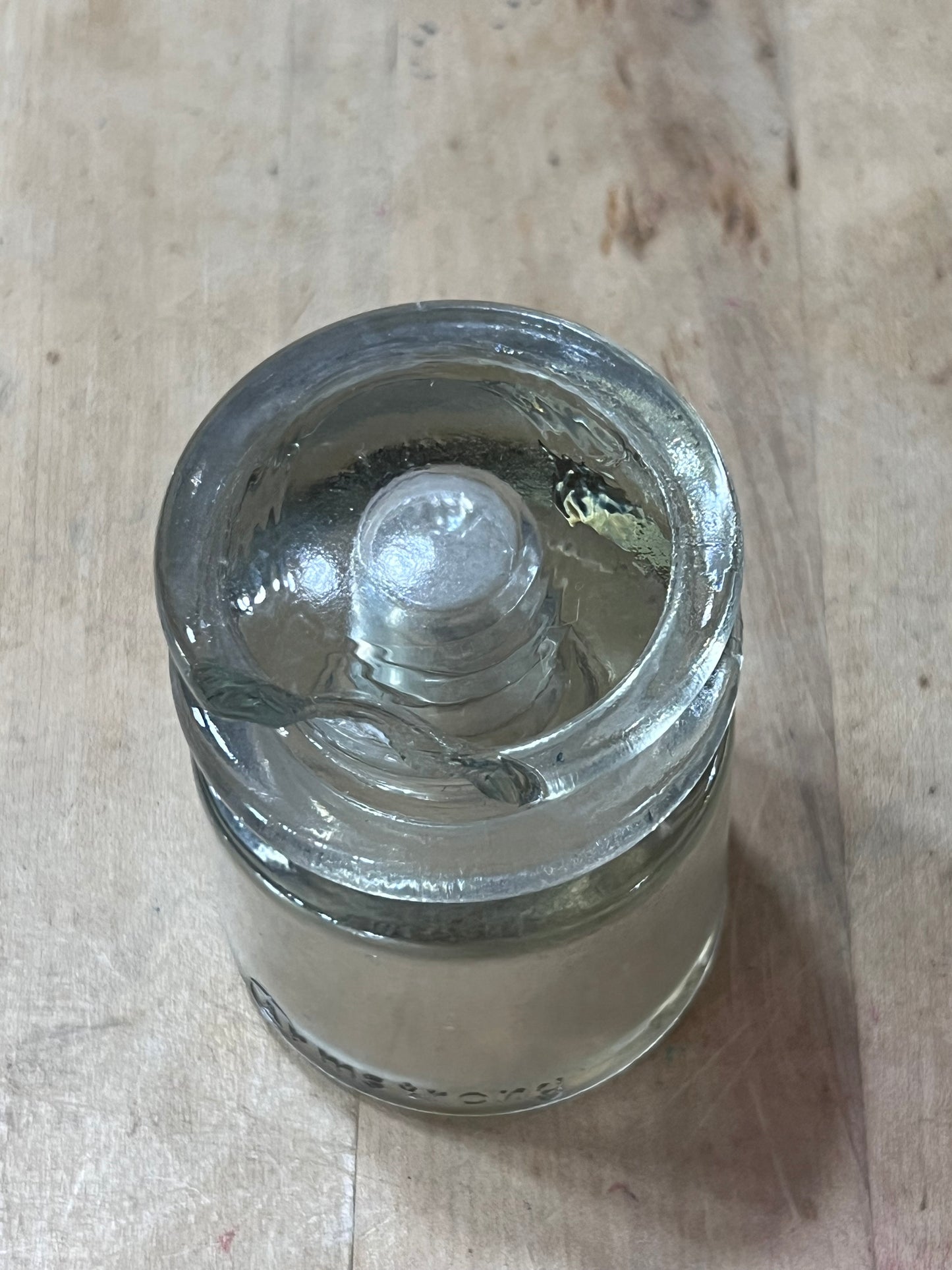 A clear glass jar with a screw-on lid, lying on its side on a light-colored wooden surface.