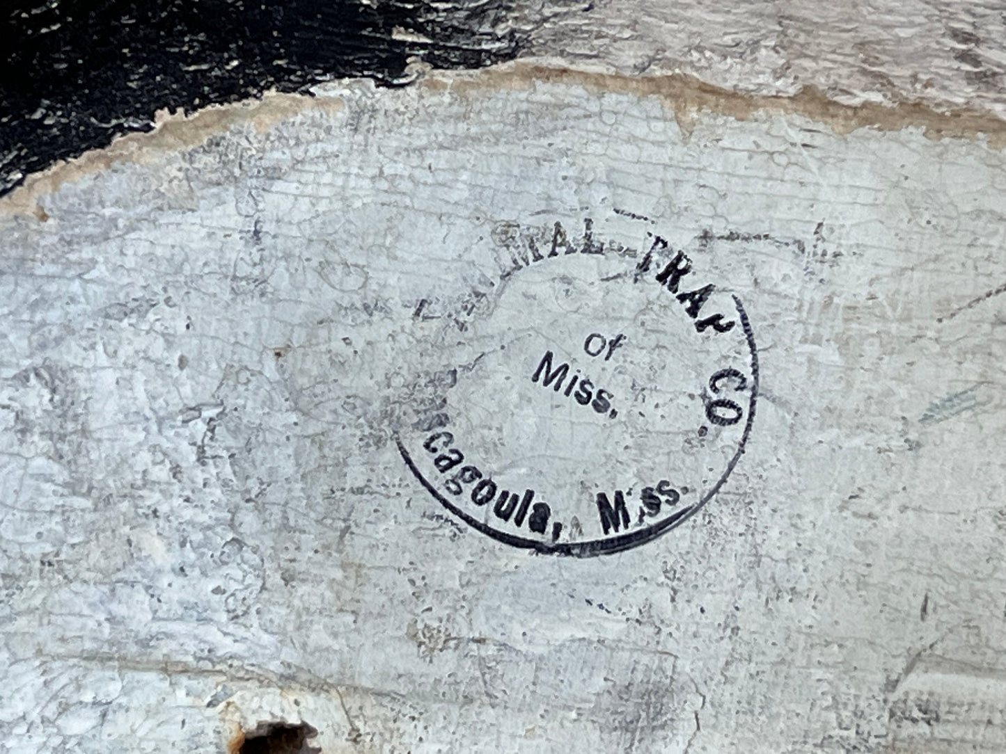 A close-up of a weathered, off-white painted surface with a circular black stamp reading 'Cargoula, Miss. of Miss.