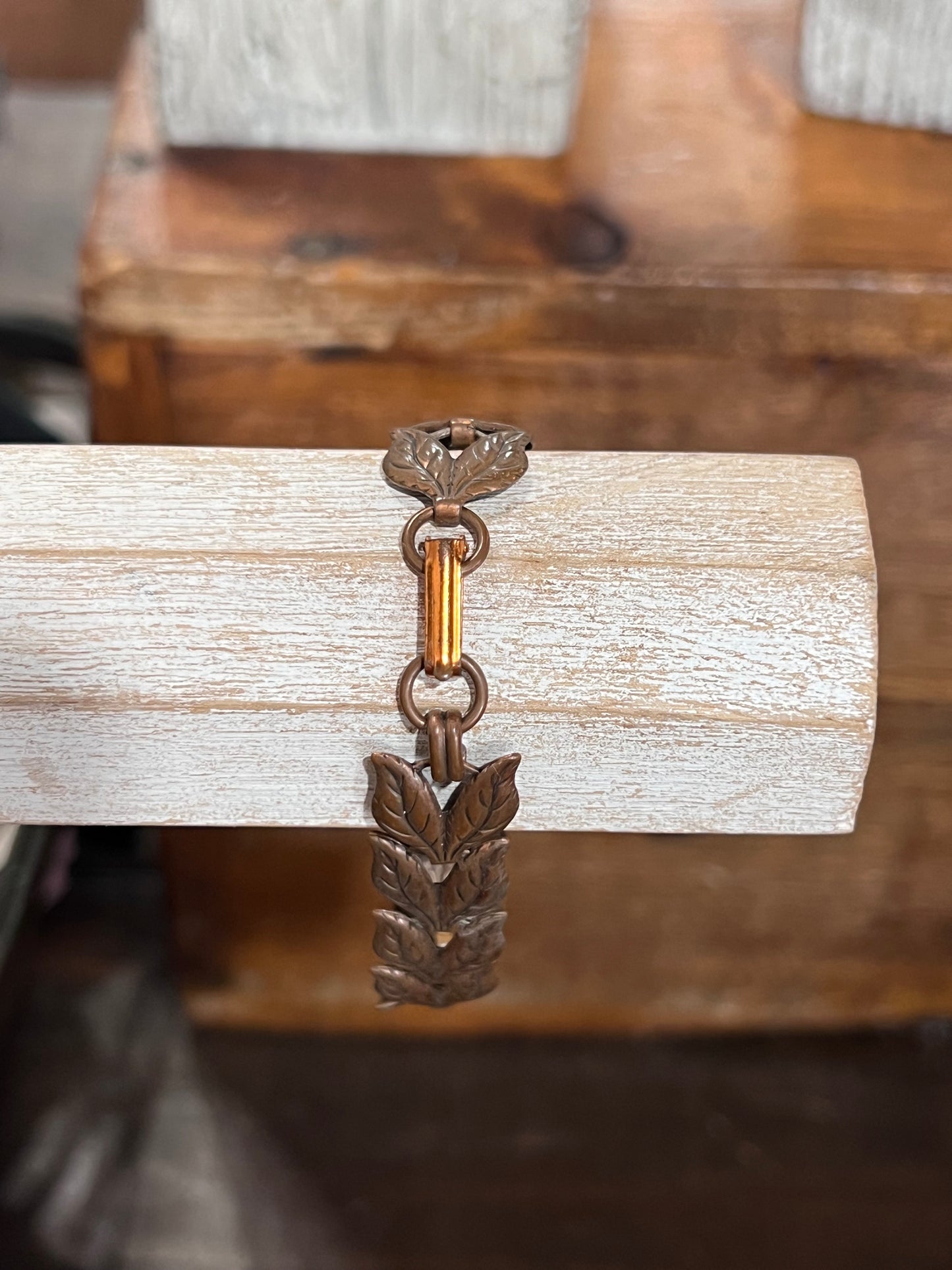 A vintage bronze-toned metal bracelet with a wheat or leaf cluster charm, displayed on a light-colored wooden block.
