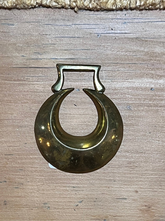 A vintage brass crescent moon ring with a rectangular top, displayed on a light-colored wooden surface.