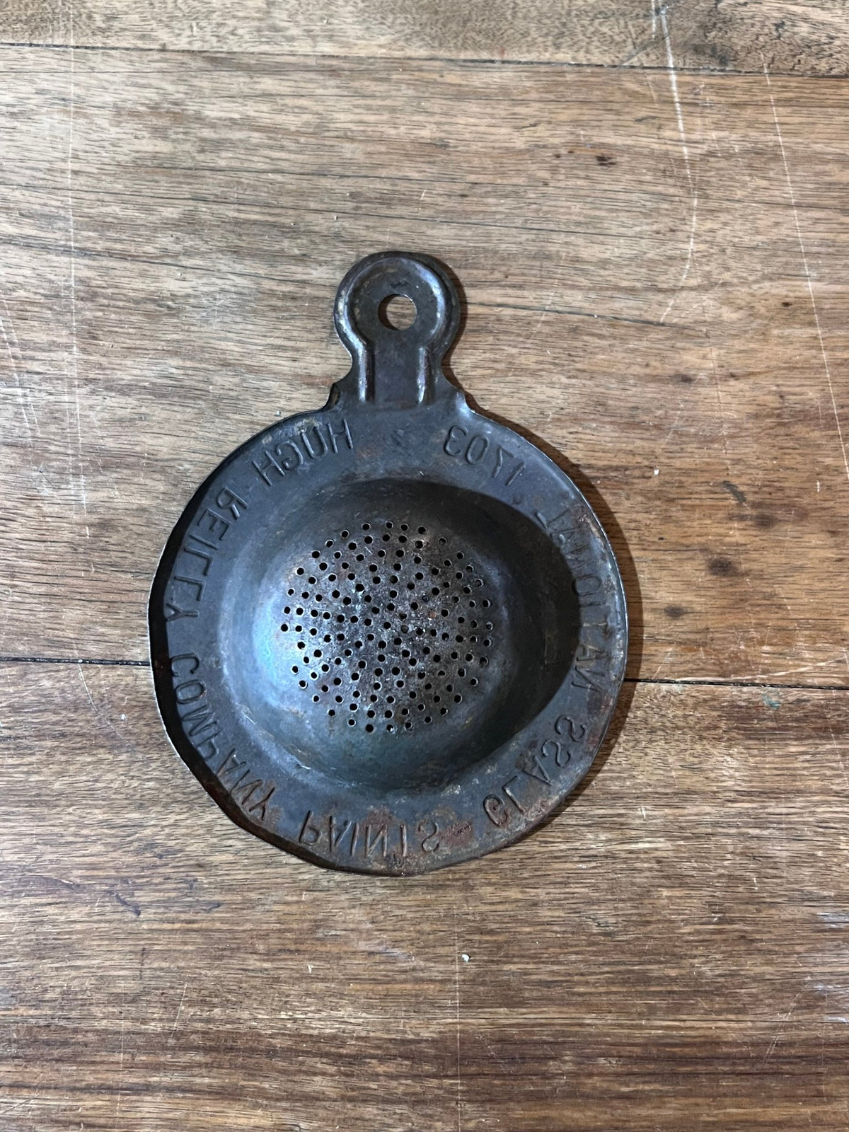A vintage metal paint strainer with embossed text, resting on a rustic wooden surface.