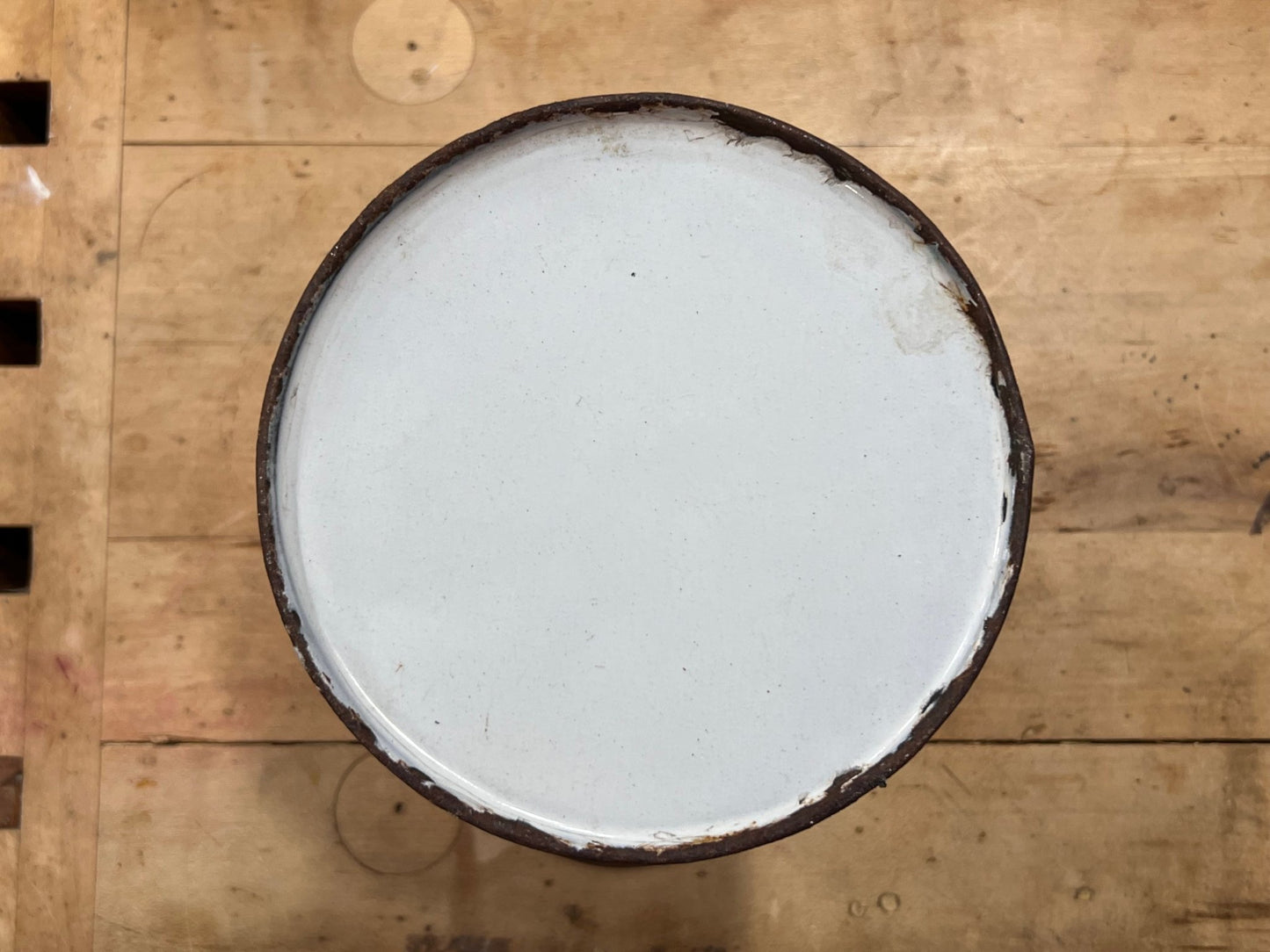 A round white enamel or plastic lid with a dark brown rim, viewed from directly above on a light brown wooden surface.