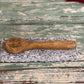 A small wooden spoon engraved with 'Taste Better' rests on a rectangular gray stone slab over a distressed green wooden surface.