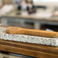 A wooden spoon rests on a rectangular speckled stone block placed on a wooden table, with a softly blurred indoor background.