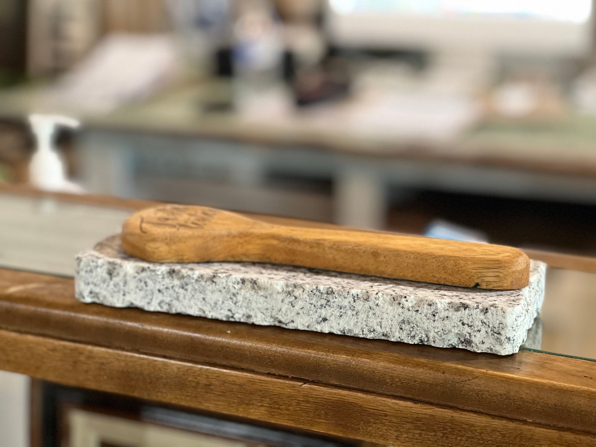 A wooden spoon rests on a rectangular speckled stone block placed on a wooden table, with a softly blurred indoor background.