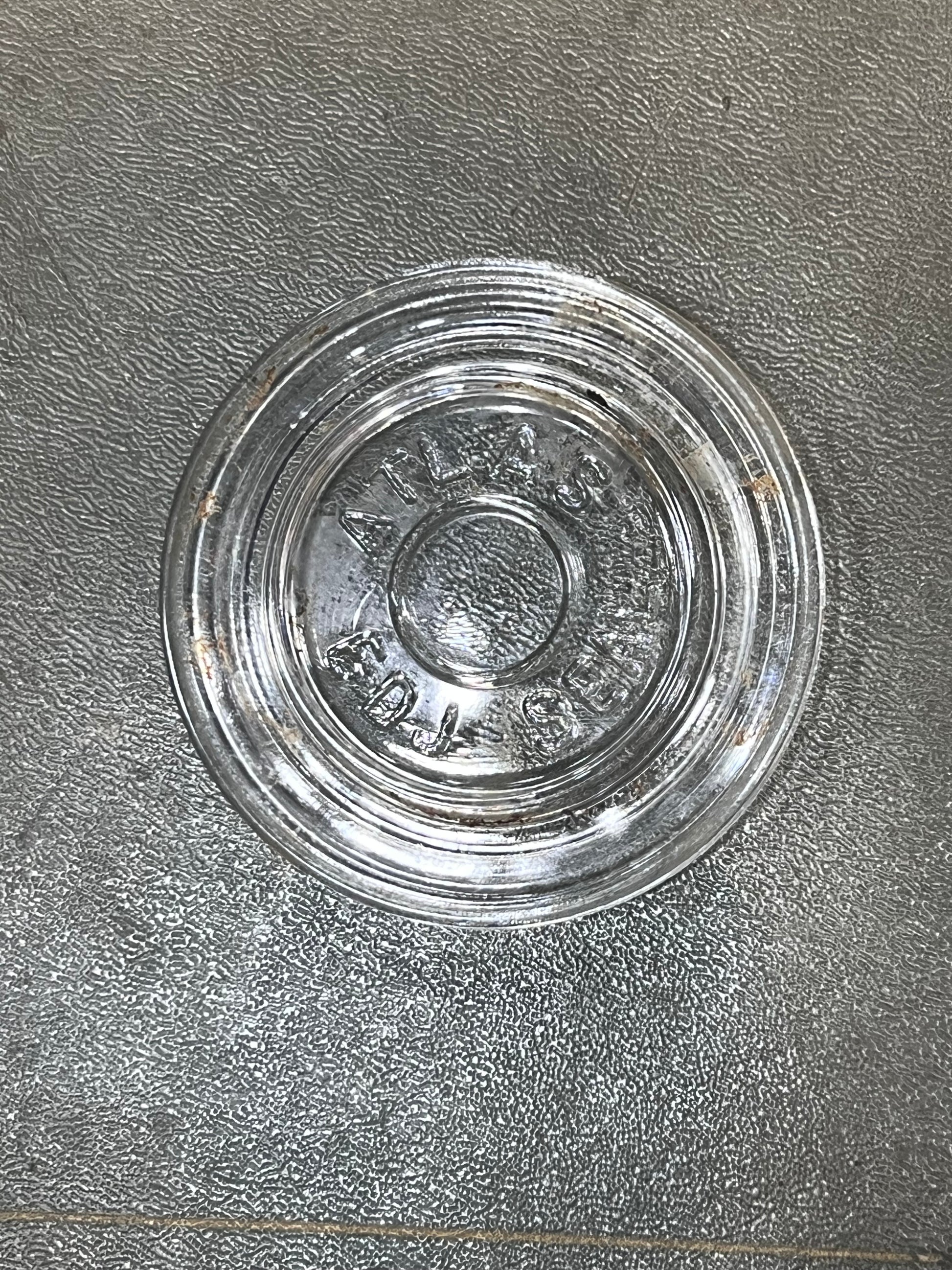 A clear glass round base or lid with embossed lettering, placed on a textured gray surface.
