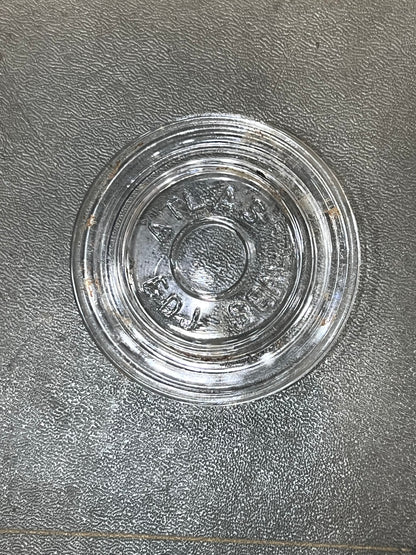 A clear glass round base or lid with embossed lettering, placed on a textured gray surface.