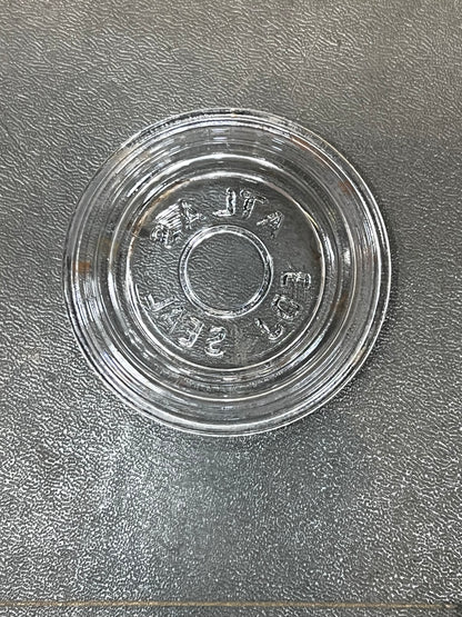 A clear glass round shallow dish or saucer with embossed text reading 'VINTA 500' on a textured gray surface.