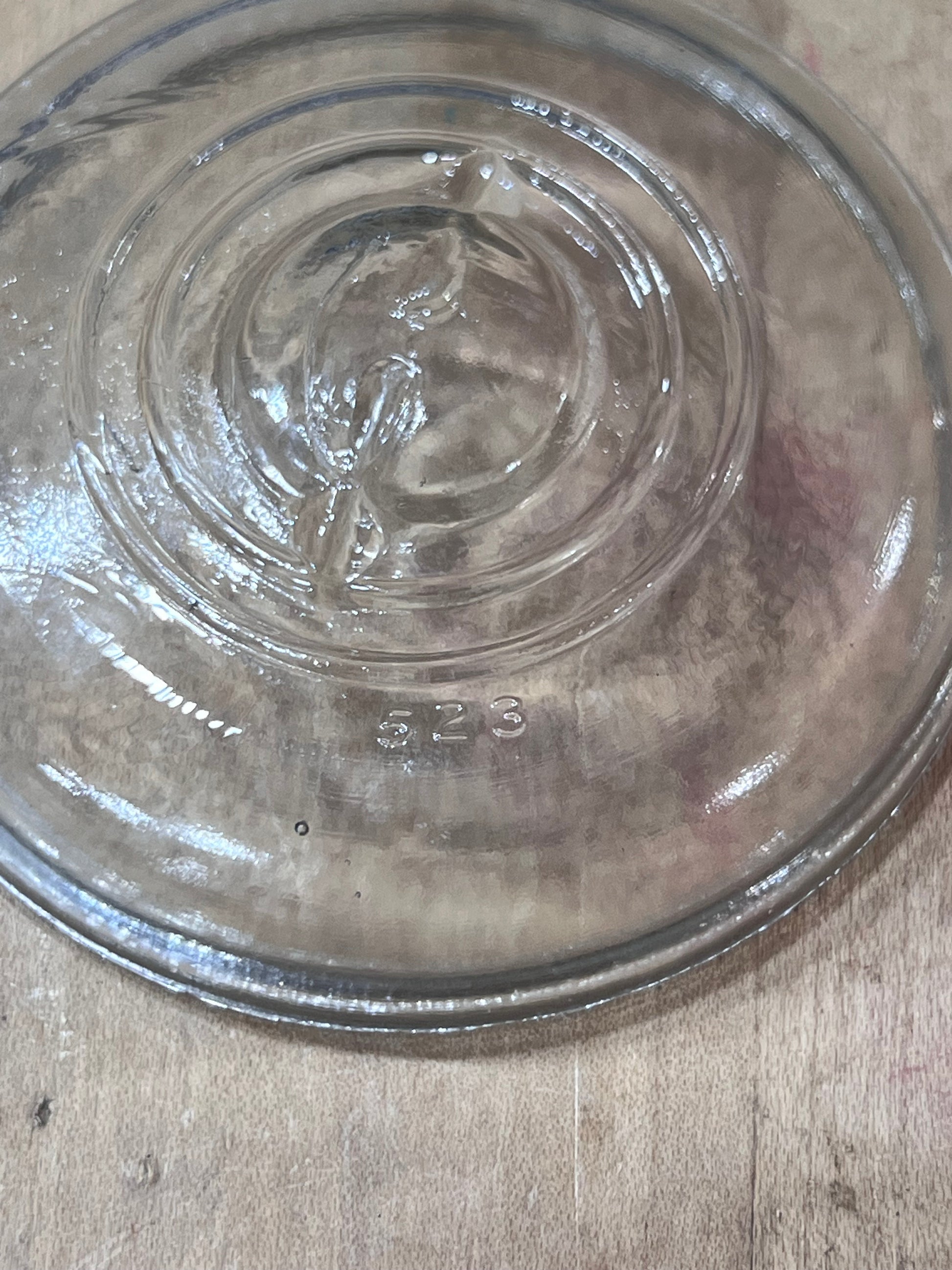 A clear glass pie dish viewed from above on a light wood surface, showing embossed measurement markings and a thick glass rim.