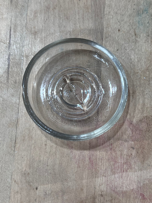 A small clear glass bowl with a thick rim, photographed from above on a worn wooden tabletop.