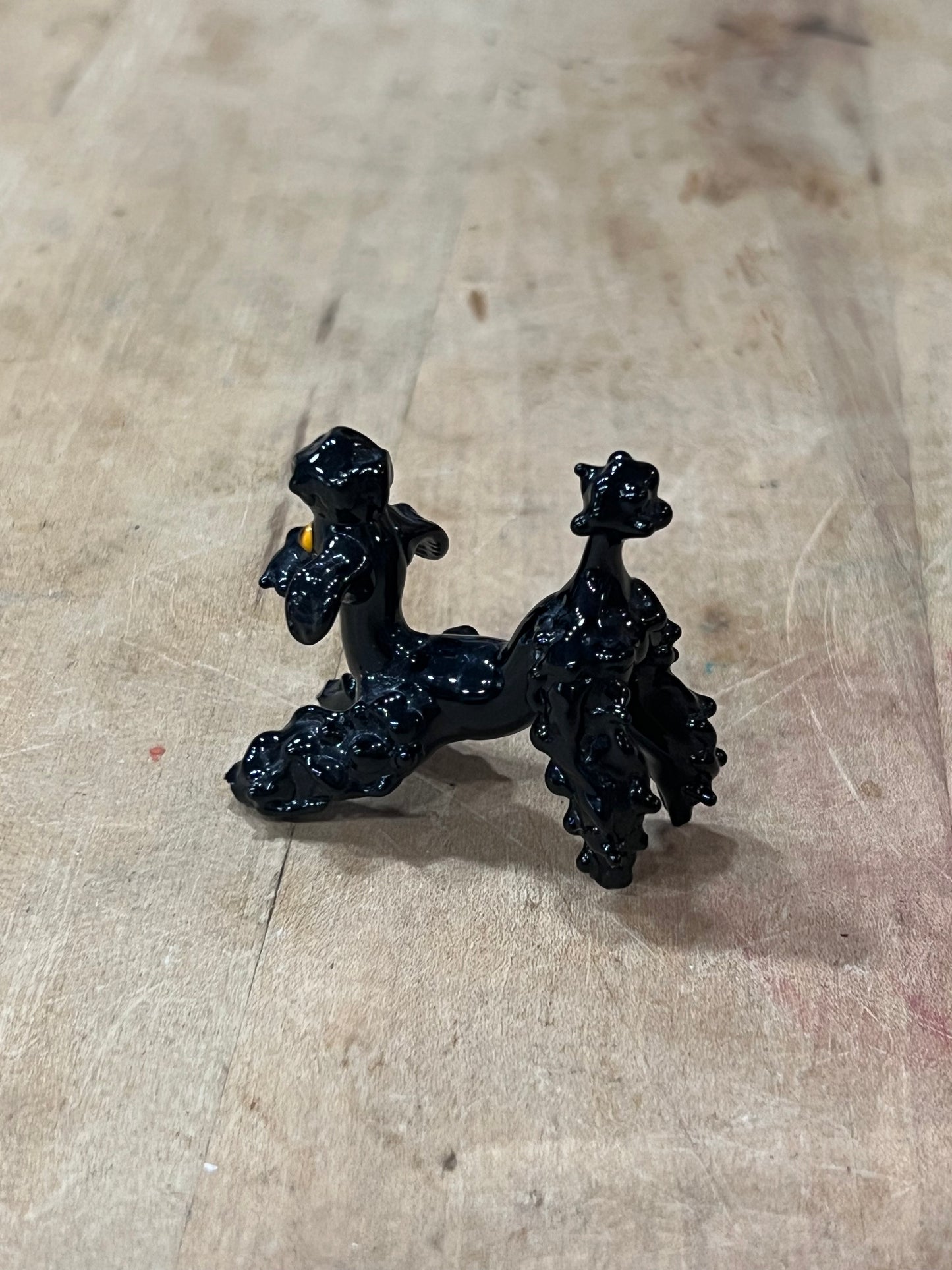 A small black decorative figurine or ornament with a glossy finish, placed on a light beige wooden surface.