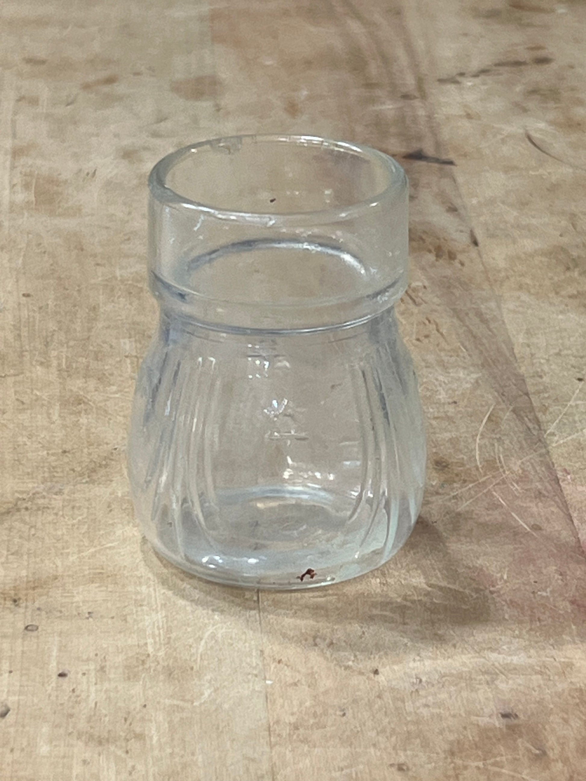 A clear glass cup with a flared rim and ribbed body, lying on a light-colored wooden surface.