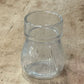 A clear glass jar or cup with a flared rim, lying on a worn beige workbench surface.
