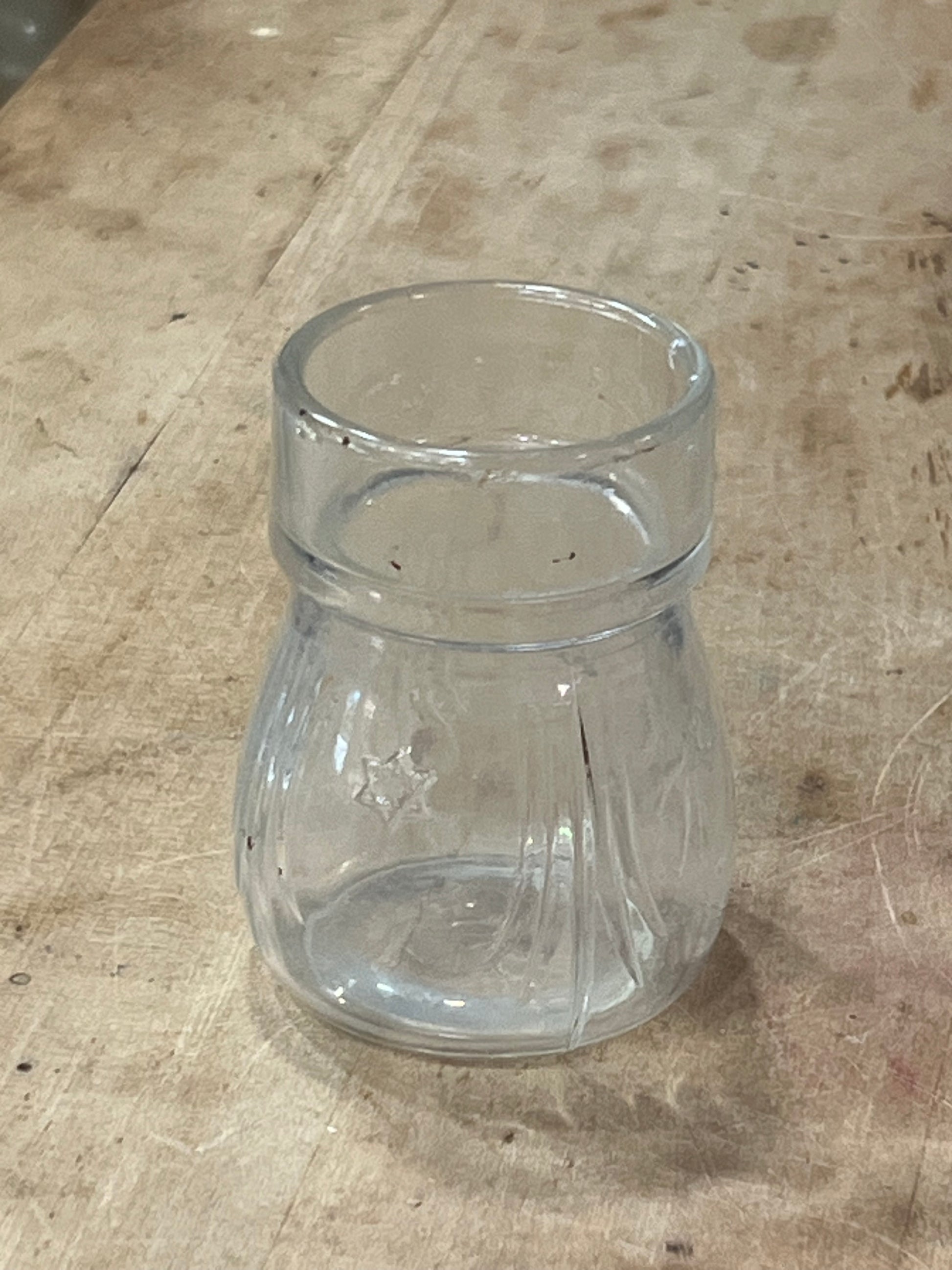 A clear glass jar or cup with a flared rim, lying on a worn beige workbench surface.