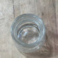 A clear glass jar with a screw-on lid, viewed from above on a light-colored wooden surface.