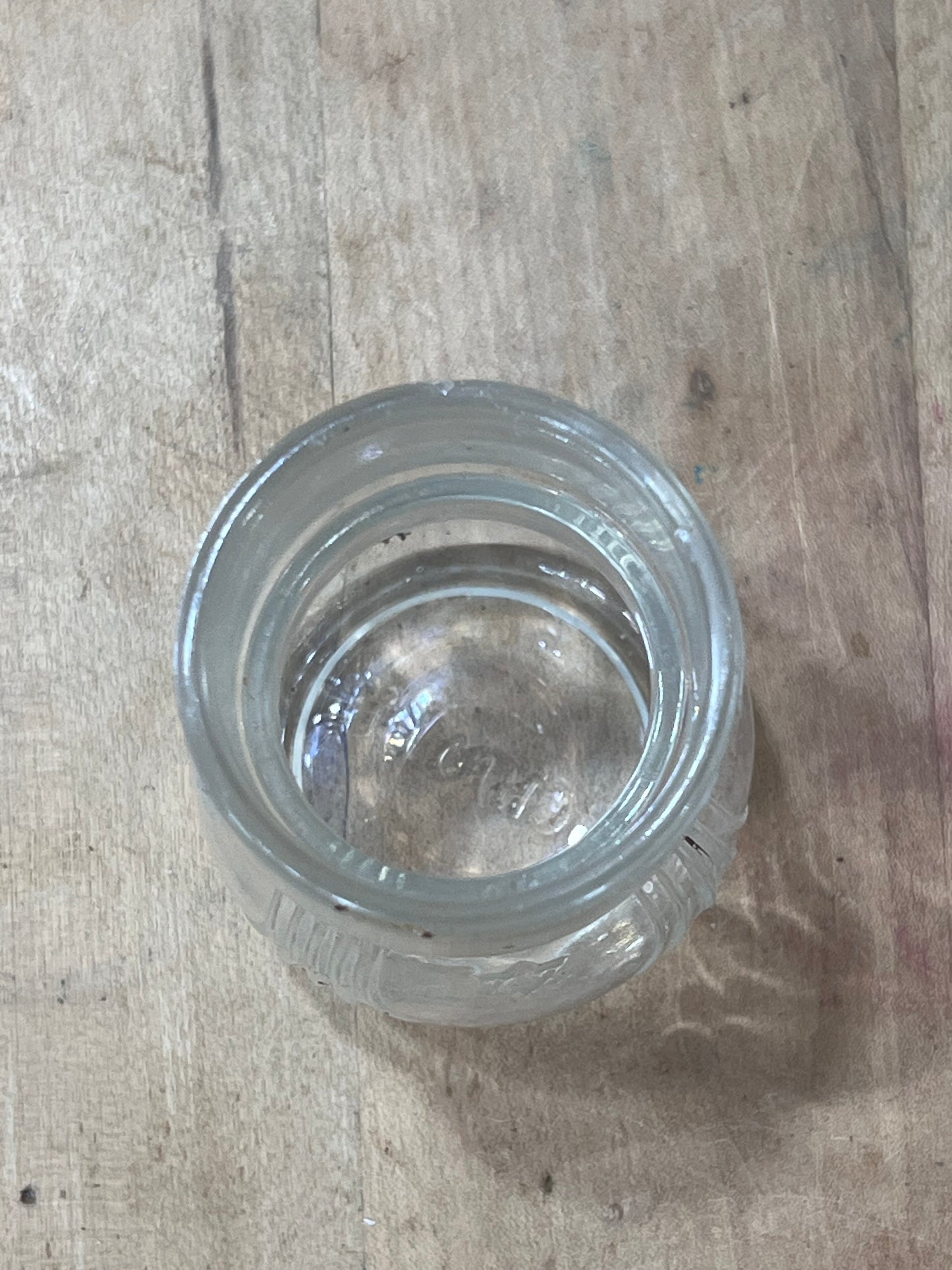 A clear glass jar with a screw-on lid, viewed from above on a light-colored wooden surface.