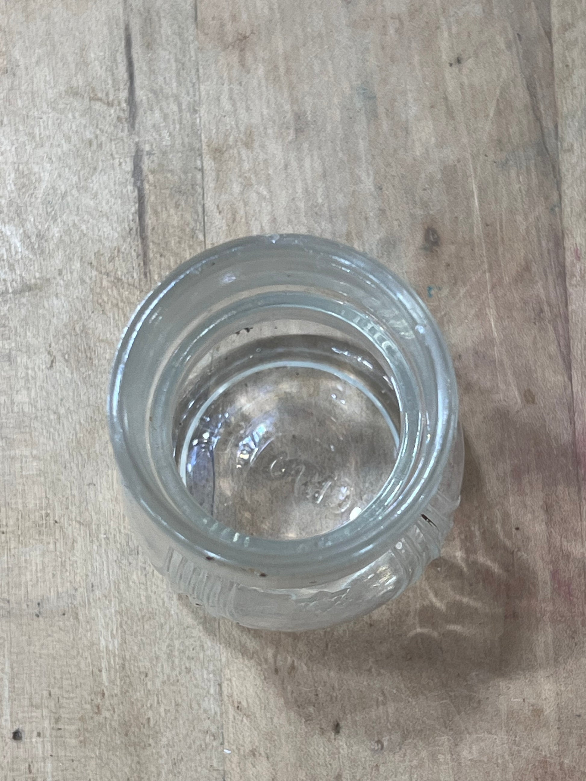 A clear glass jar with a screw-on lid, viewed from above on a light-colored wooden surface.