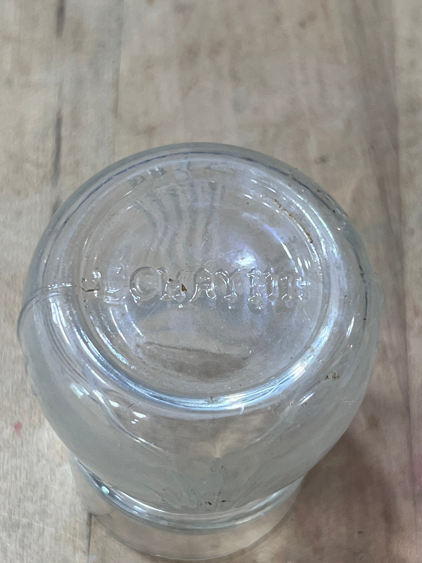 A clear glass jar viewed from above, showing the embossed brand name 'Oster' on the glass base, resting on a light-colored wooden surface.