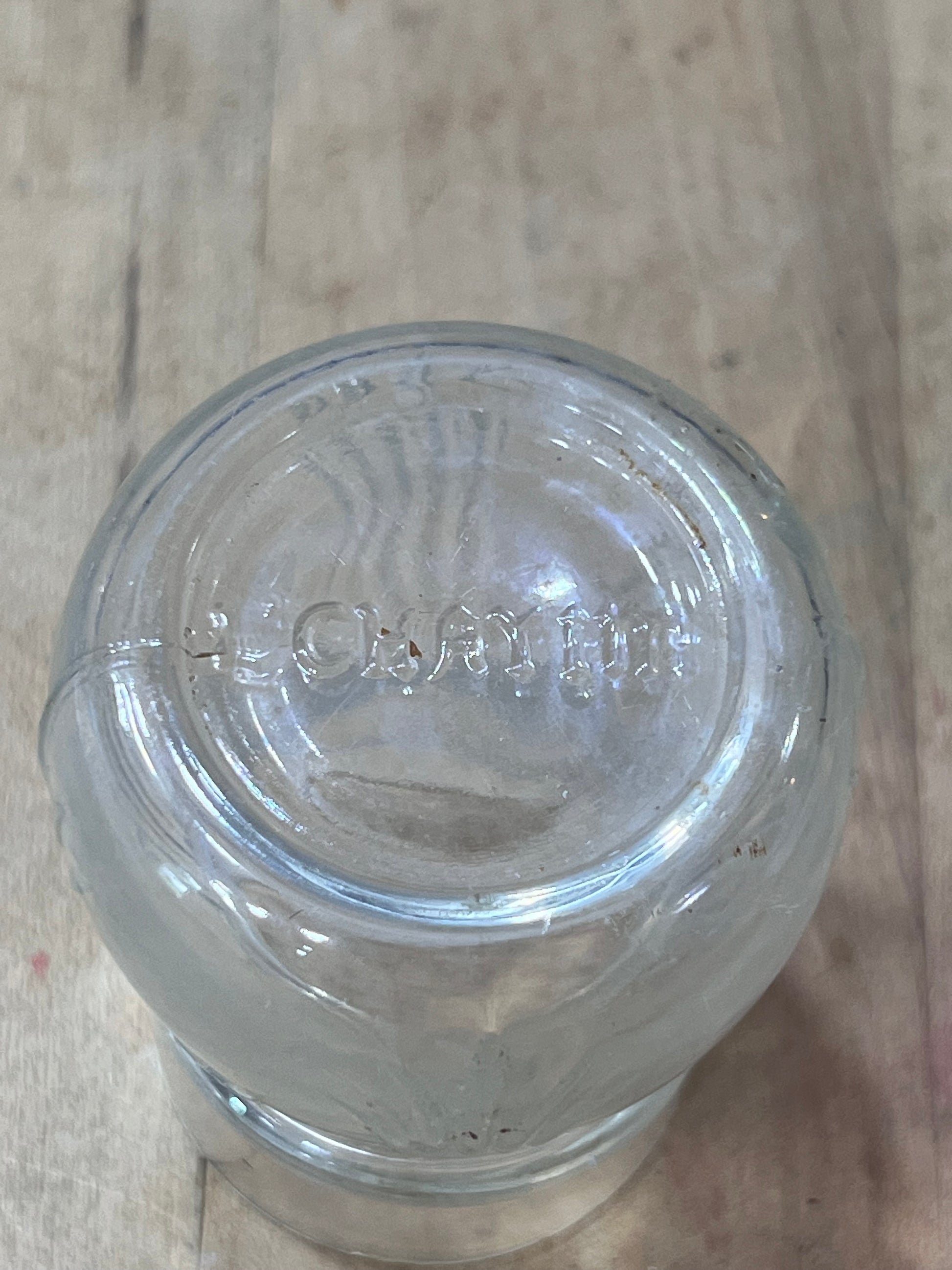 A clear glass jar viewed from above, showing the embossed brand name 'Oster' on the glass base, resting on a light-colored wooden surface.