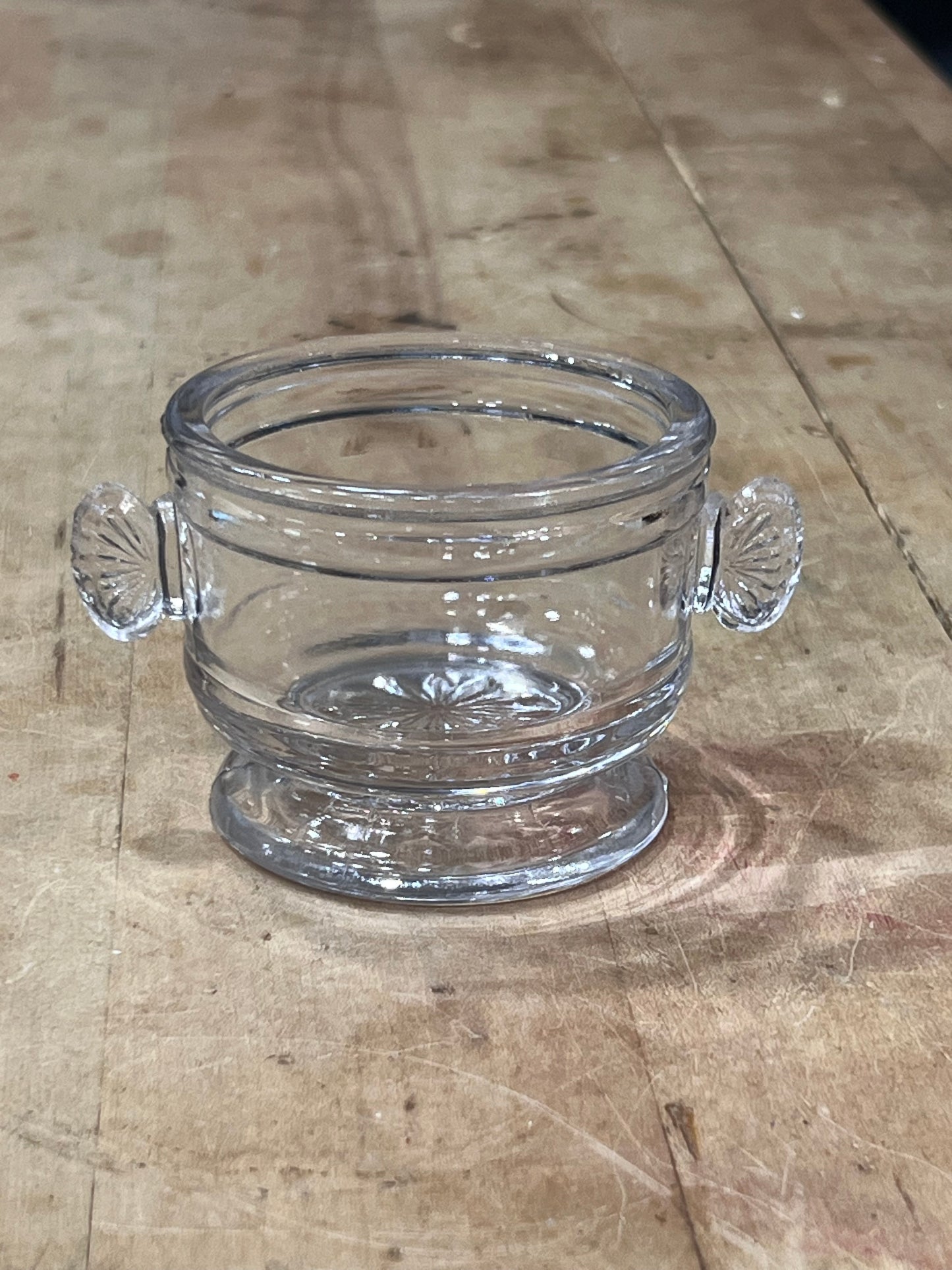 A clear glass bowl with decorative scalloped handles, shown on a rustic wooden surface.