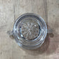 A clear glass ashtray with a floral starburst pattern on the bottom, shown from a top-down view on a light wood surface.