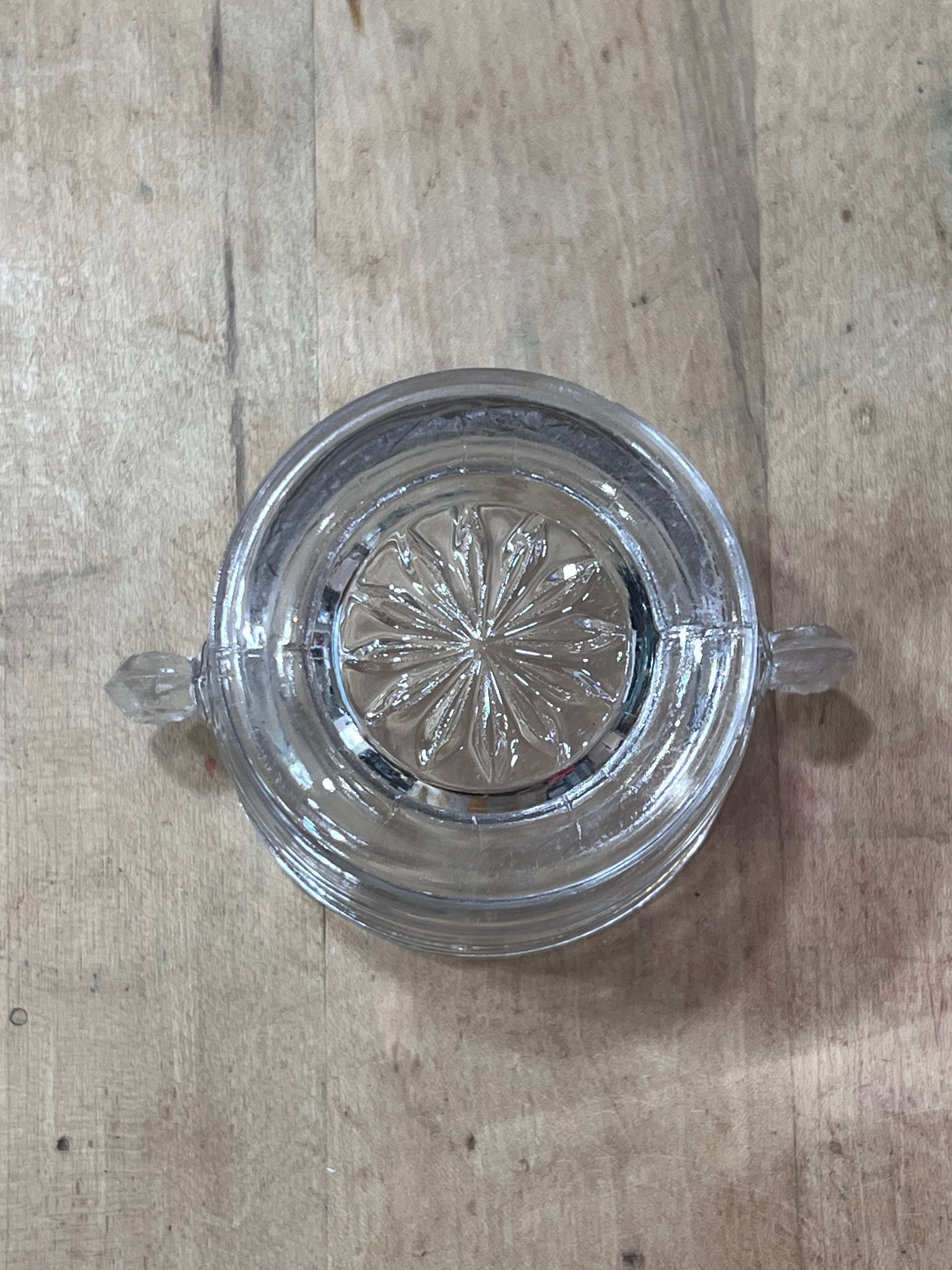 A clear glass ashtray with a floral starburst pattern on the bottom, shown from a top-down view on a light wood surface.