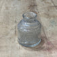 A small clear glass bottle with a ribbed textured body and a short neck, lying on a light-colored wooden surface.