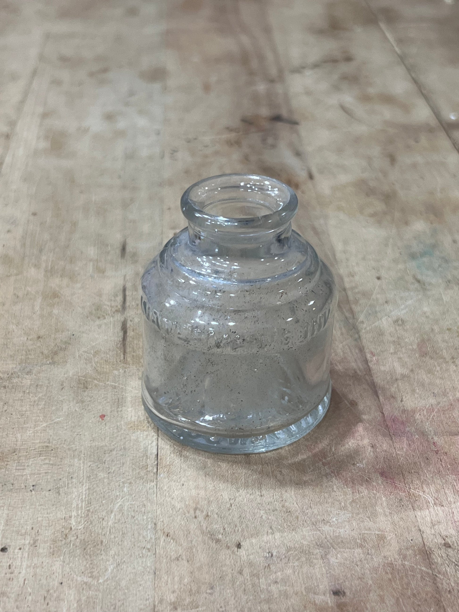 A small clear glass bottle with a ribbed textured body and a short neck, lying on a light-colored wooden surface.