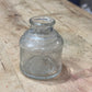 A small, empty clear glass jar with a ribbed shoulder and a short neck, lying on a worn wooden surface.