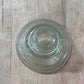 A clear glass bowl or saucer with a concentric ring design, photographed from above on a light wood surface.
