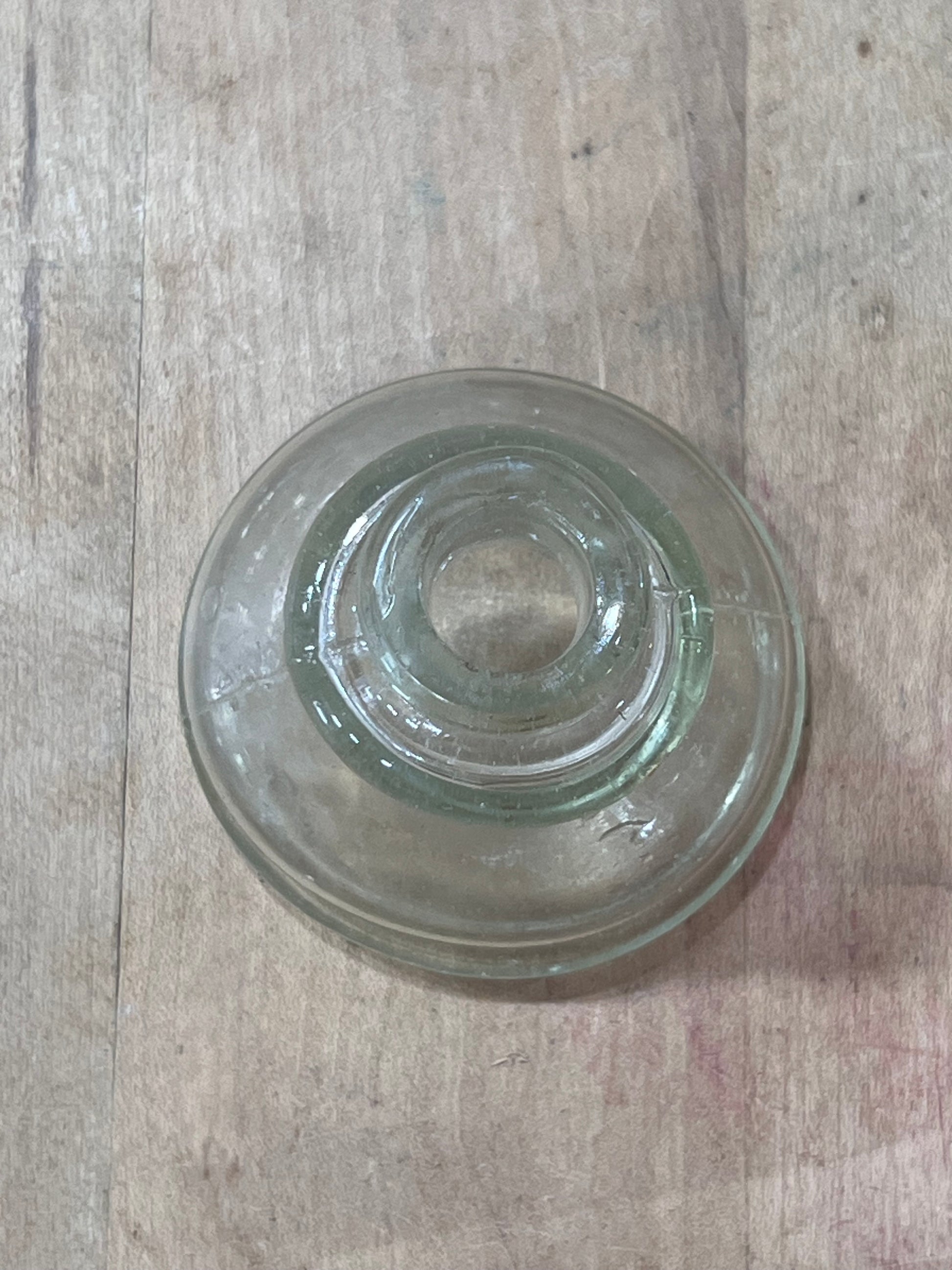 A clear glass bowl or saucer with a concentric ring design, photographed from above on a light wood surface.