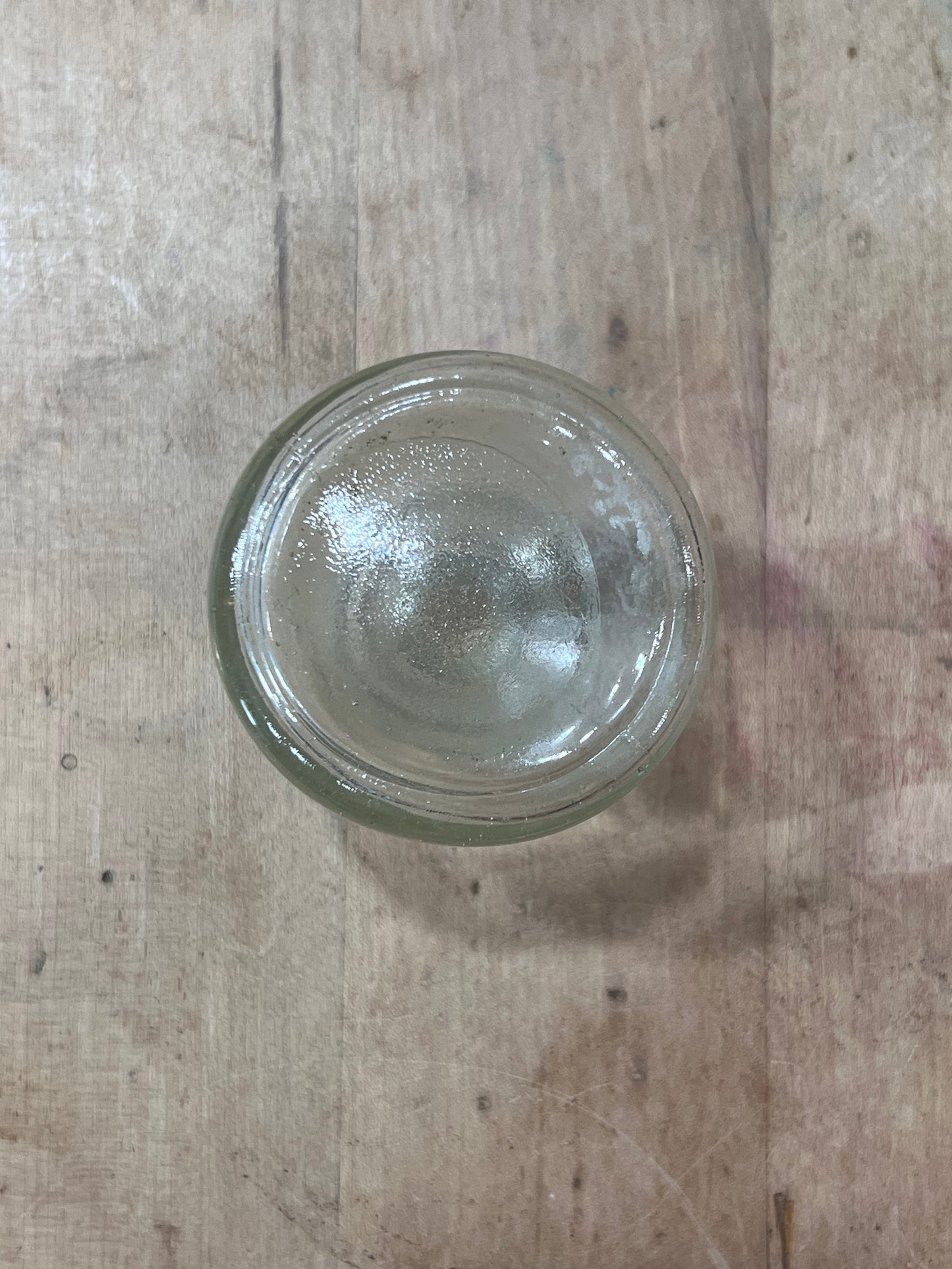A small, round, clear glass jar or bowl viewed from directly above on a rustic wooden surface.