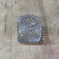 A small clear glass or plastic textured container with a circular opening, placed on a worn wooden surface.