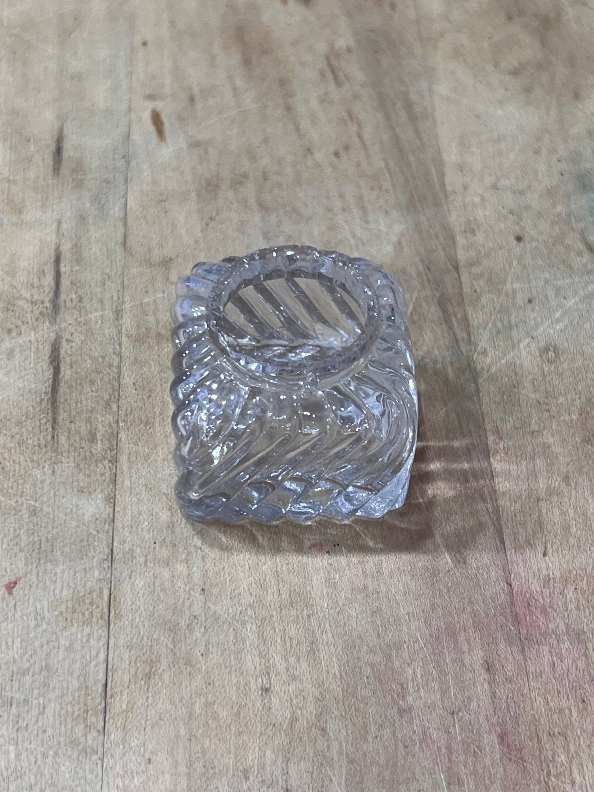 A small clear glass or plastic textured container with a circular opening, placed on a worn wooden surface.