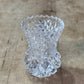 A clear cut-crystal or glass vase with a textured, faceted pattern, photographed from above on a rustic wooden surface.