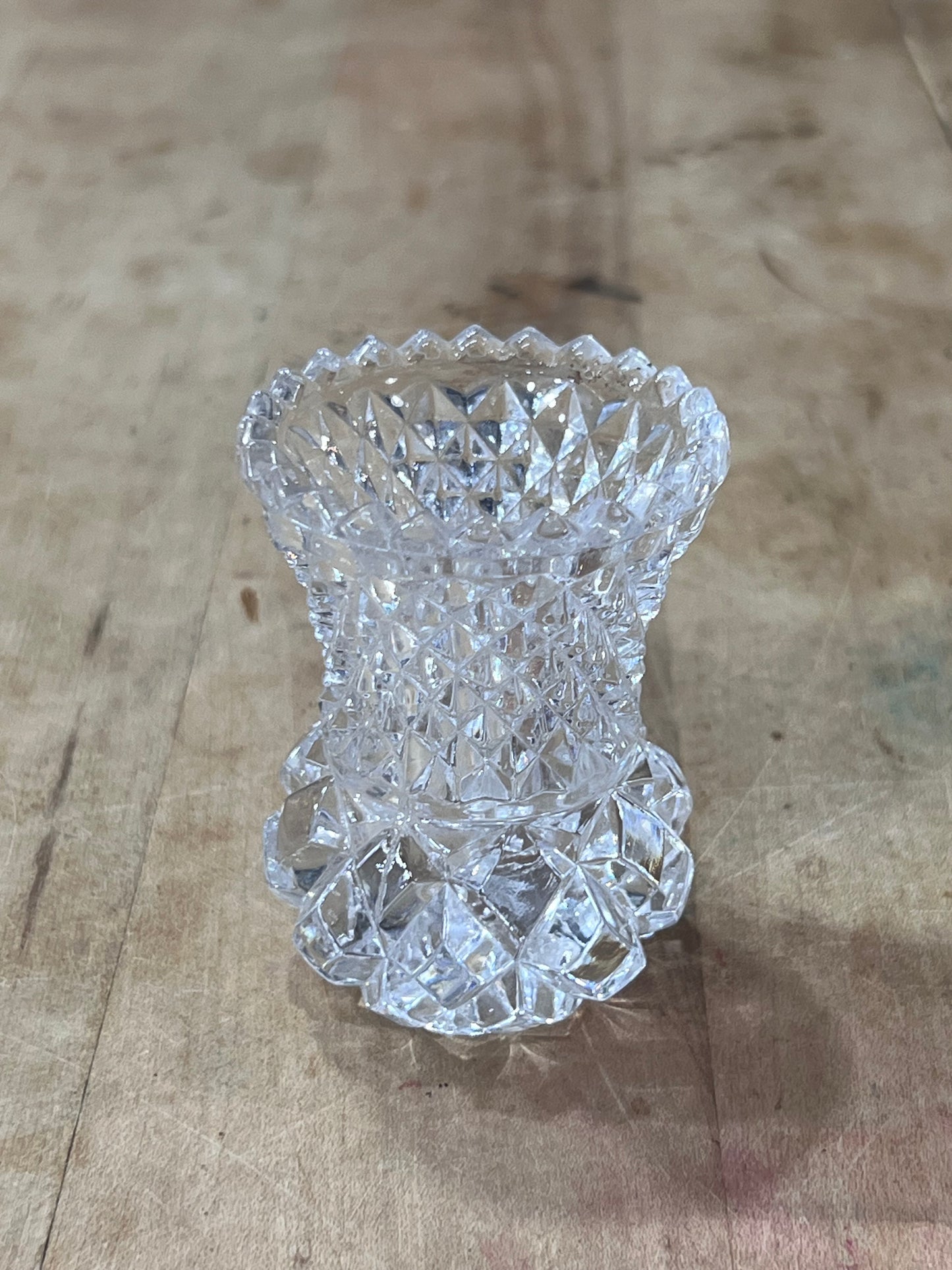 A clear cut-crystal or glass vase with a textured, faceted pattern, photographed from above on a rustic wooden surface.