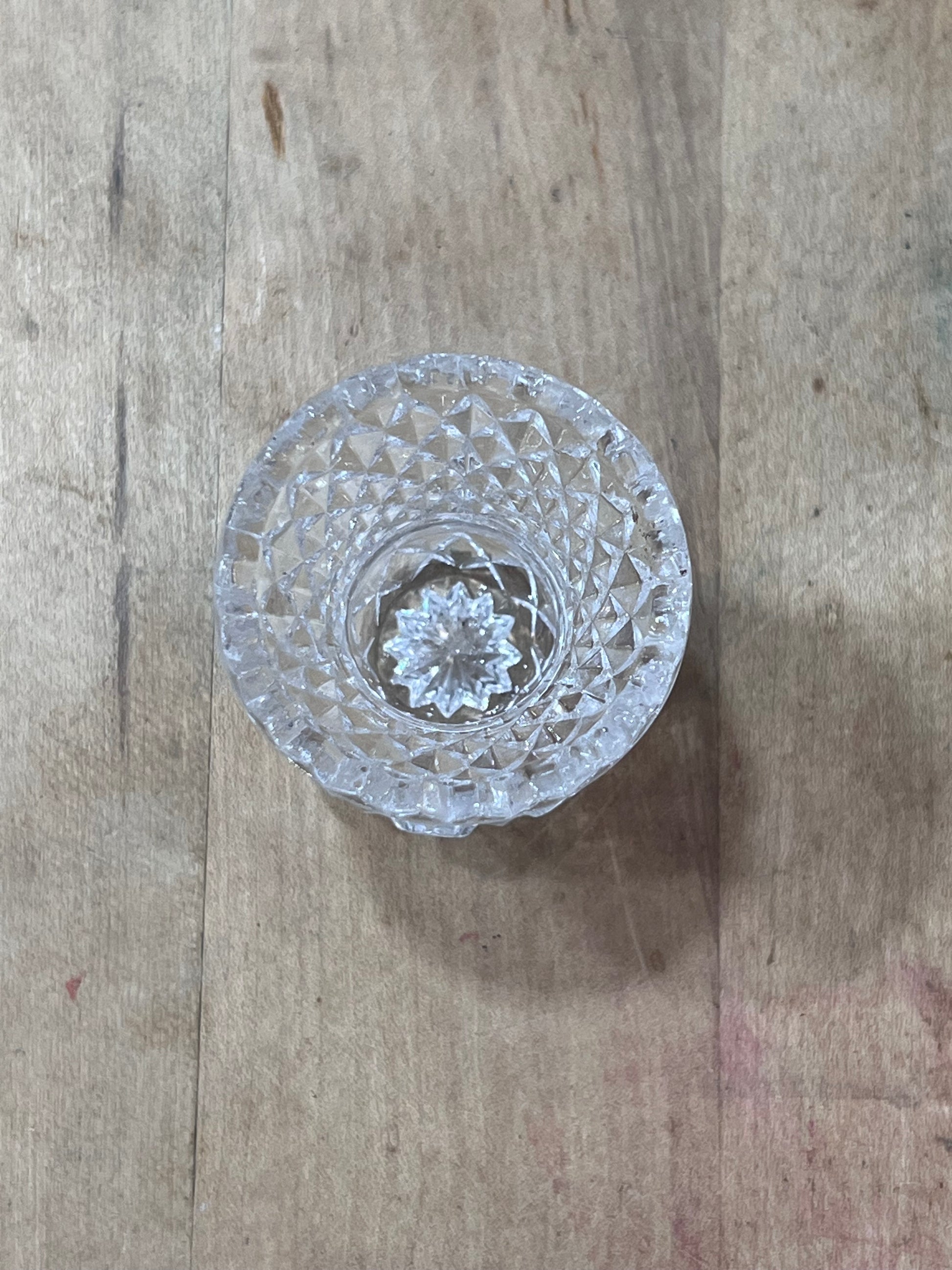 A clear cut-crystal or glass tumbler viewed from above, resting on a rustic wooden surface.
