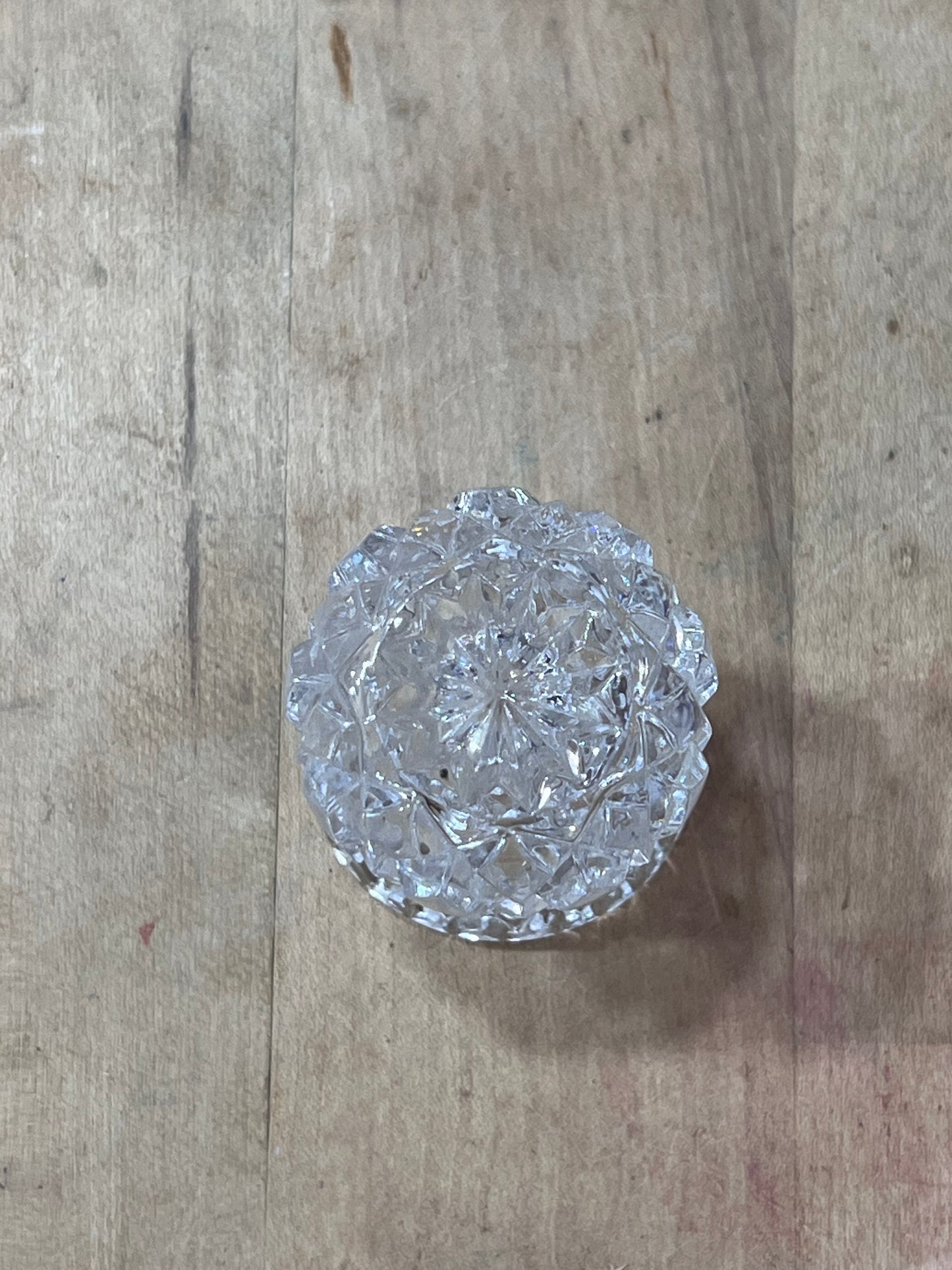 A round, faceted clear glass or crystal dish with a textured, cut pattern, resting on a light-colored wooden surface.