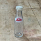 A clear glass bottle with a white screw cap and a white label featuring red Arabic script, lying on a worn wooden surface.
