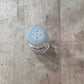 A small clear plastic bottle with a translucent white cap and red printed text, lying on a worn wooden surface.