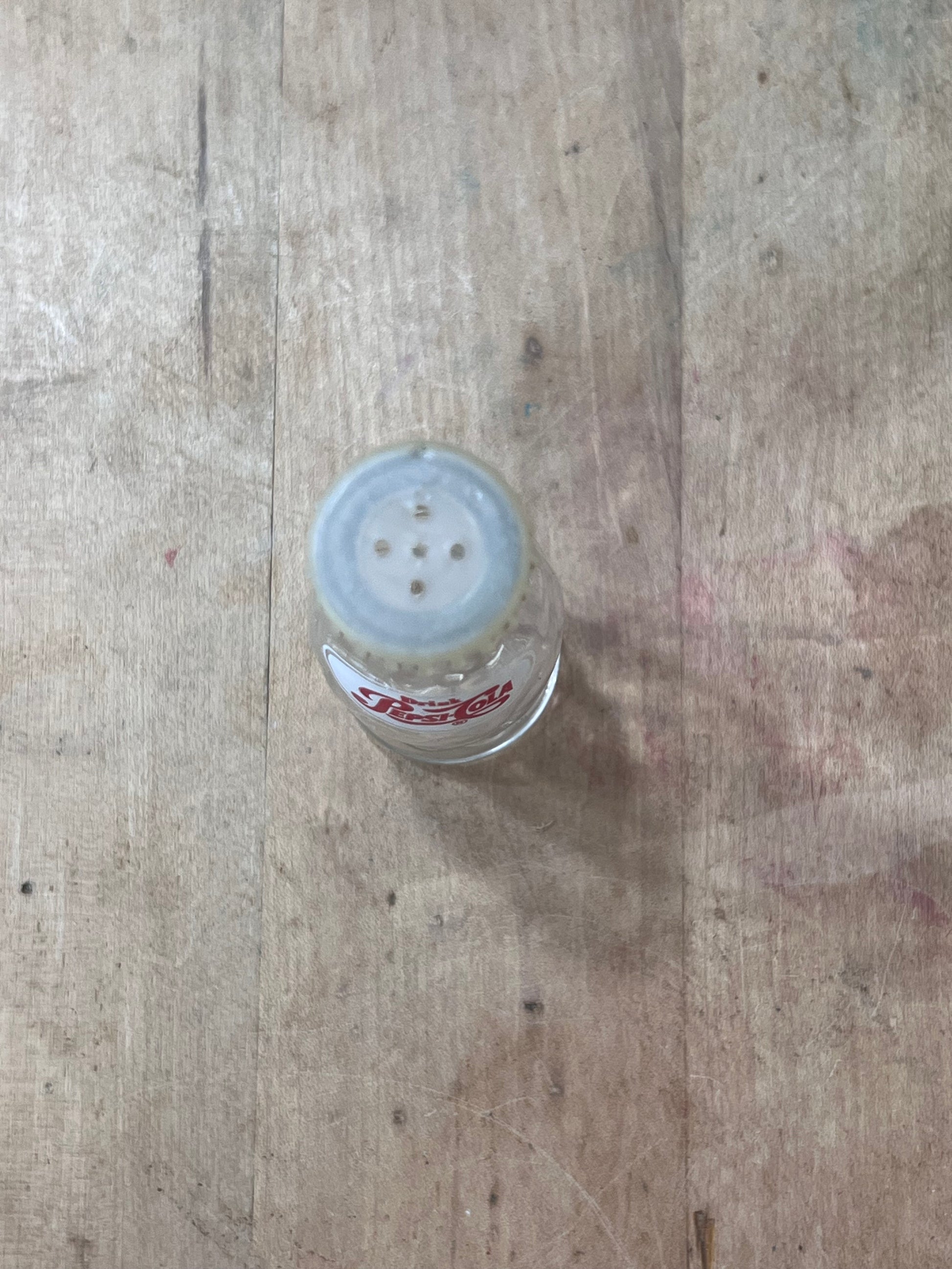 A small clear plastic bottle with a translucent white cap and red printed text, lying on a worn wooden surface.