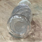 A clear glass bottle with a ribbed screw cap, lying on a textured beige surface.