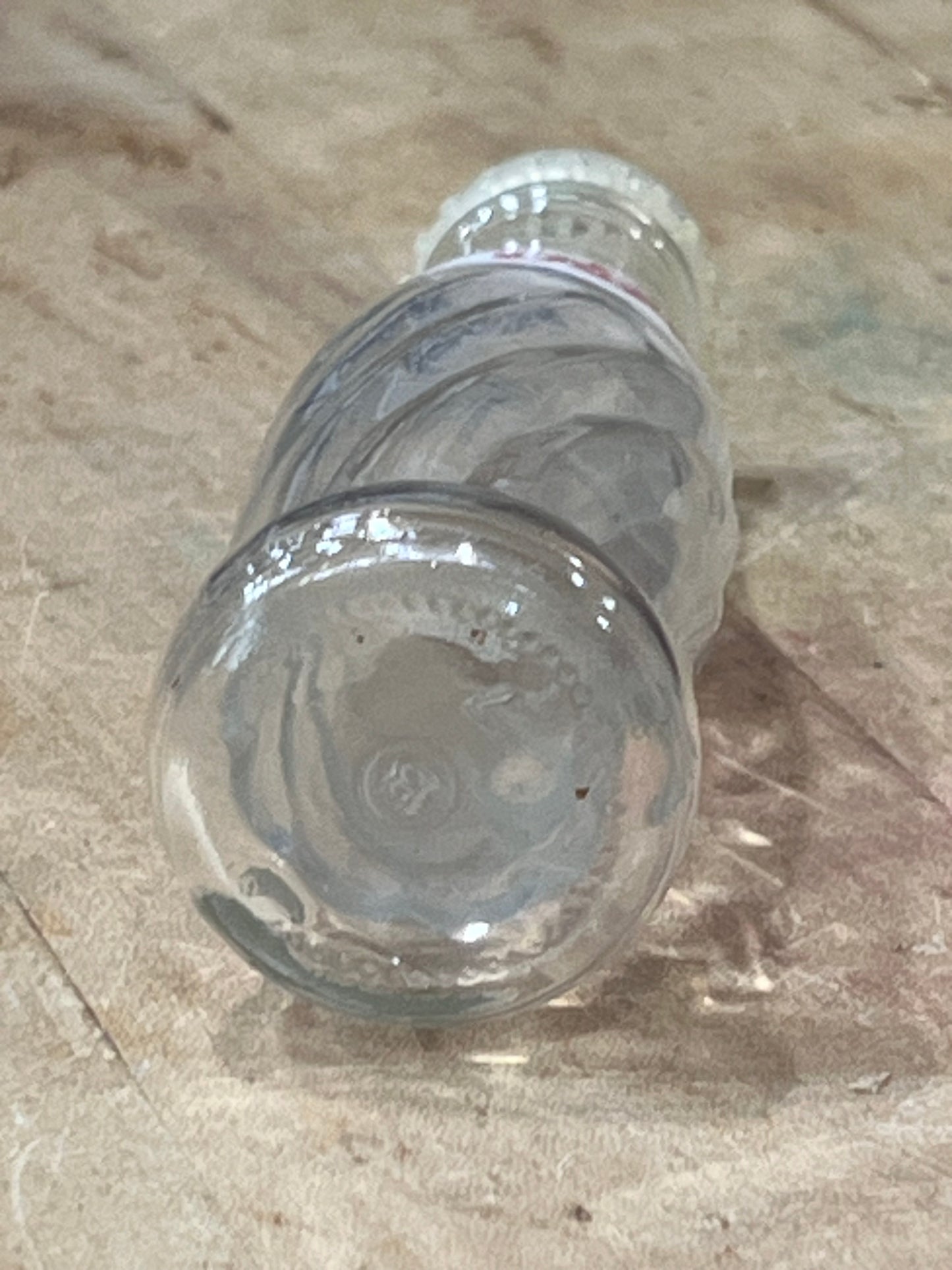 A clear glass bottle with a ribbed screw cap, lying on a textured beige surface.