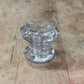 A clear glass cabinet knob with a faceted, ribbed pattern, resting on a light brown wooden surface.
