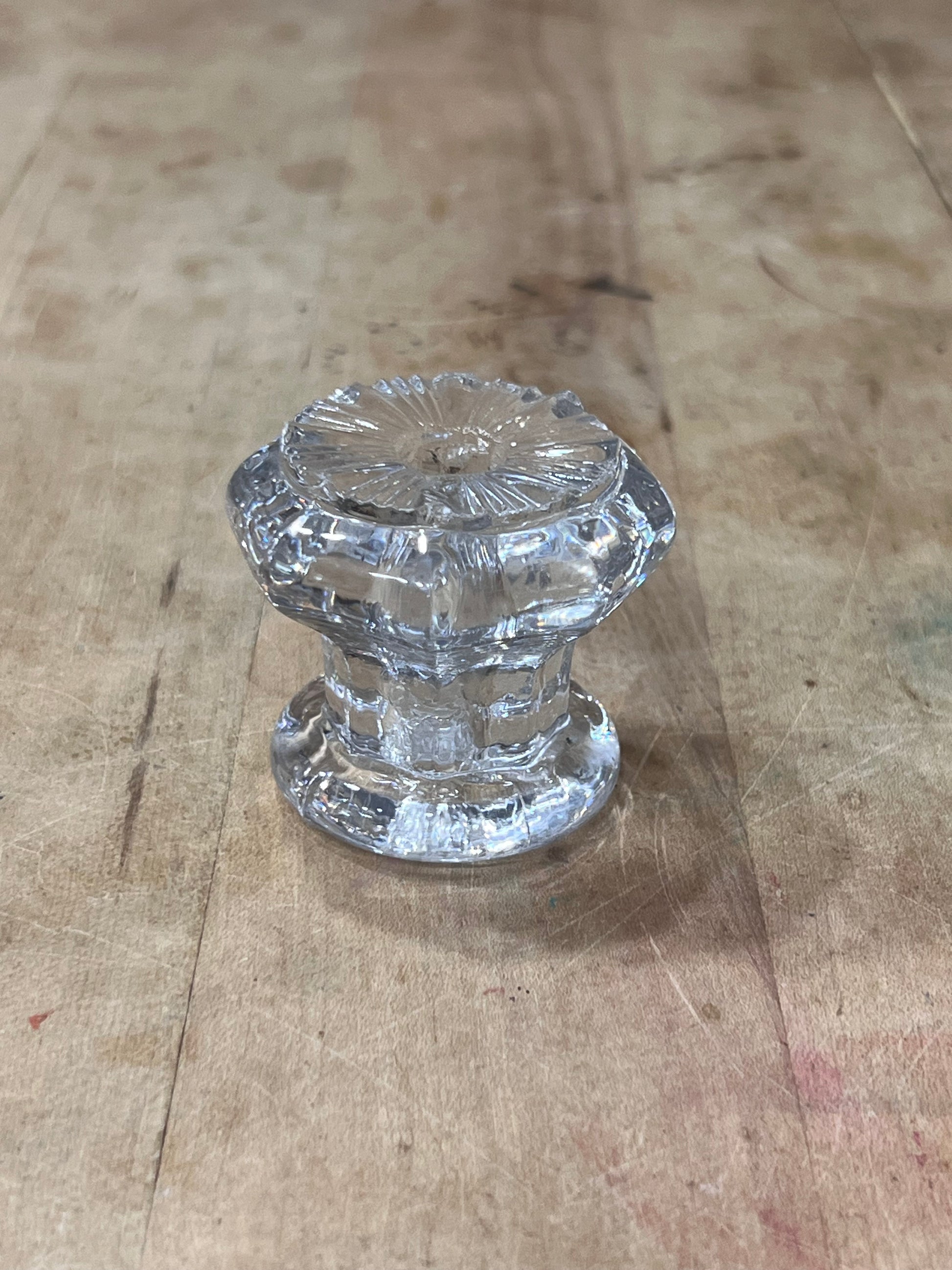 A clear glass cabinet knob with a faceted, ribbed pattern, resting on a light brown wooden surface.