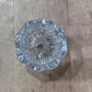 A clear glass or acrylic cut crystal knob with a faceted, starburst pattern, photographed from above on a rustic wooden surface.
