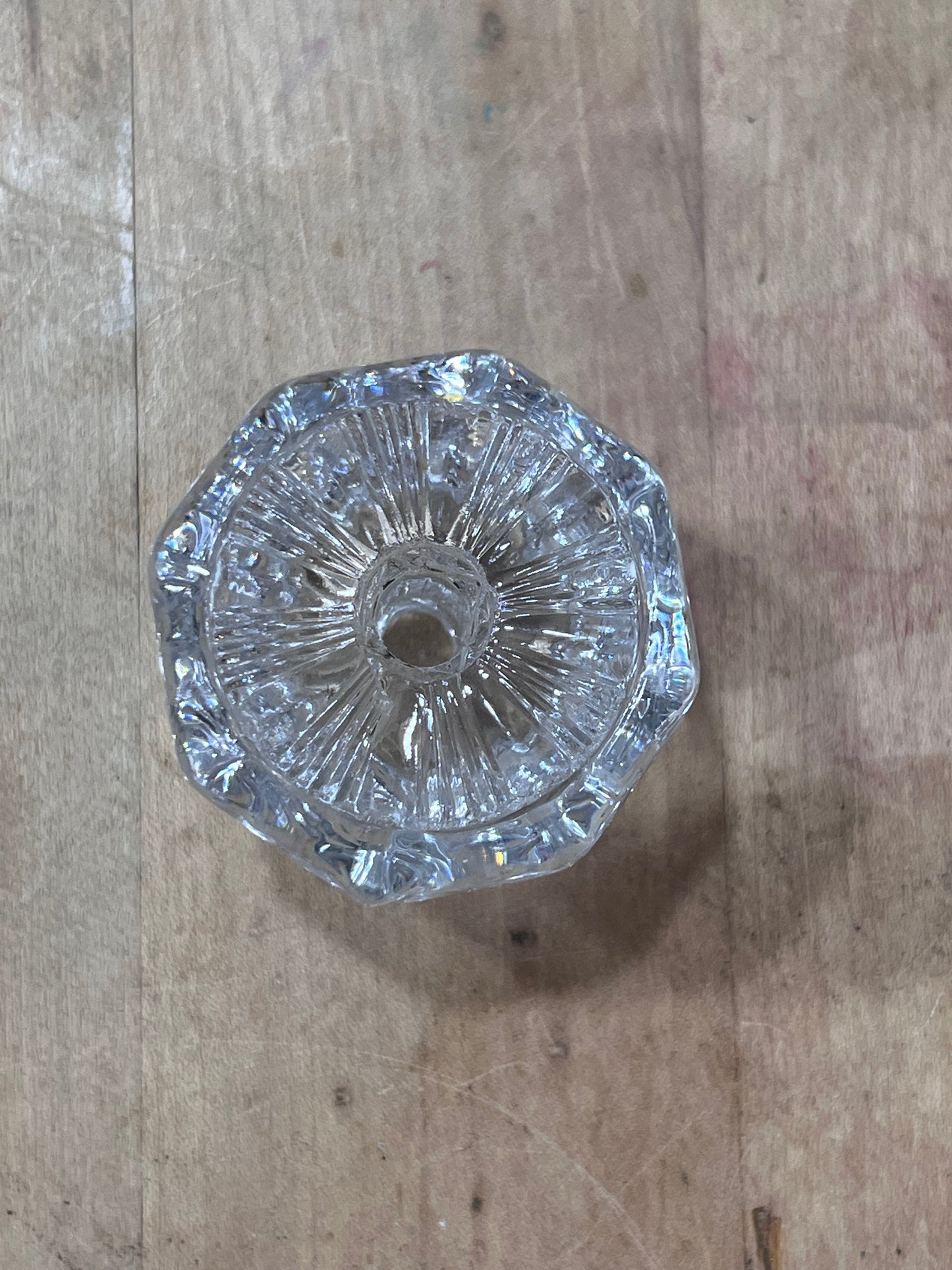 A clear glass or acrylic cut crystal knob with a faceted, starburst pattern, photographed from above on a rustic wooden surface.