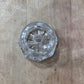 A small clear glass or acrylic decorative object with a faceted circular design, placed on a light brown wooden surface.
