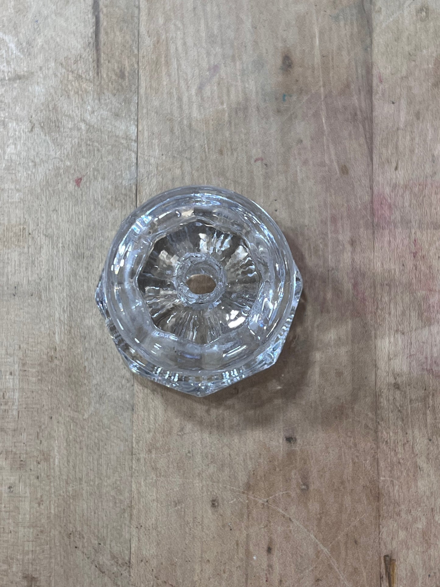 A small clear glass or acrylic decorative object with a faceted circular design, placed on a light brown wooden surface.