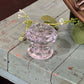 A vintage-style clear glass doorknob with a faceted, starburst pattern, mounted on a distressed, light blue-gray wooden cabinet with decorative greenery.